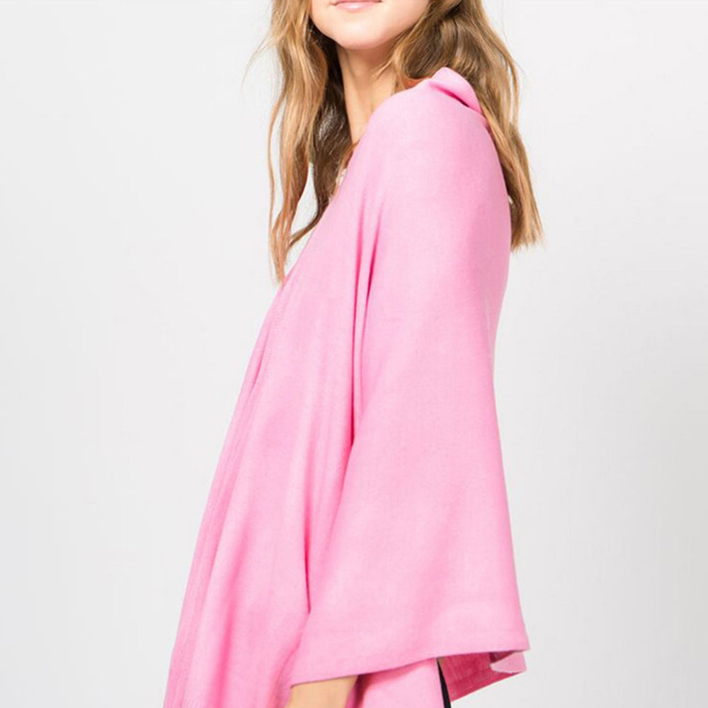 Young woman standing from the side wearing a pink poncho